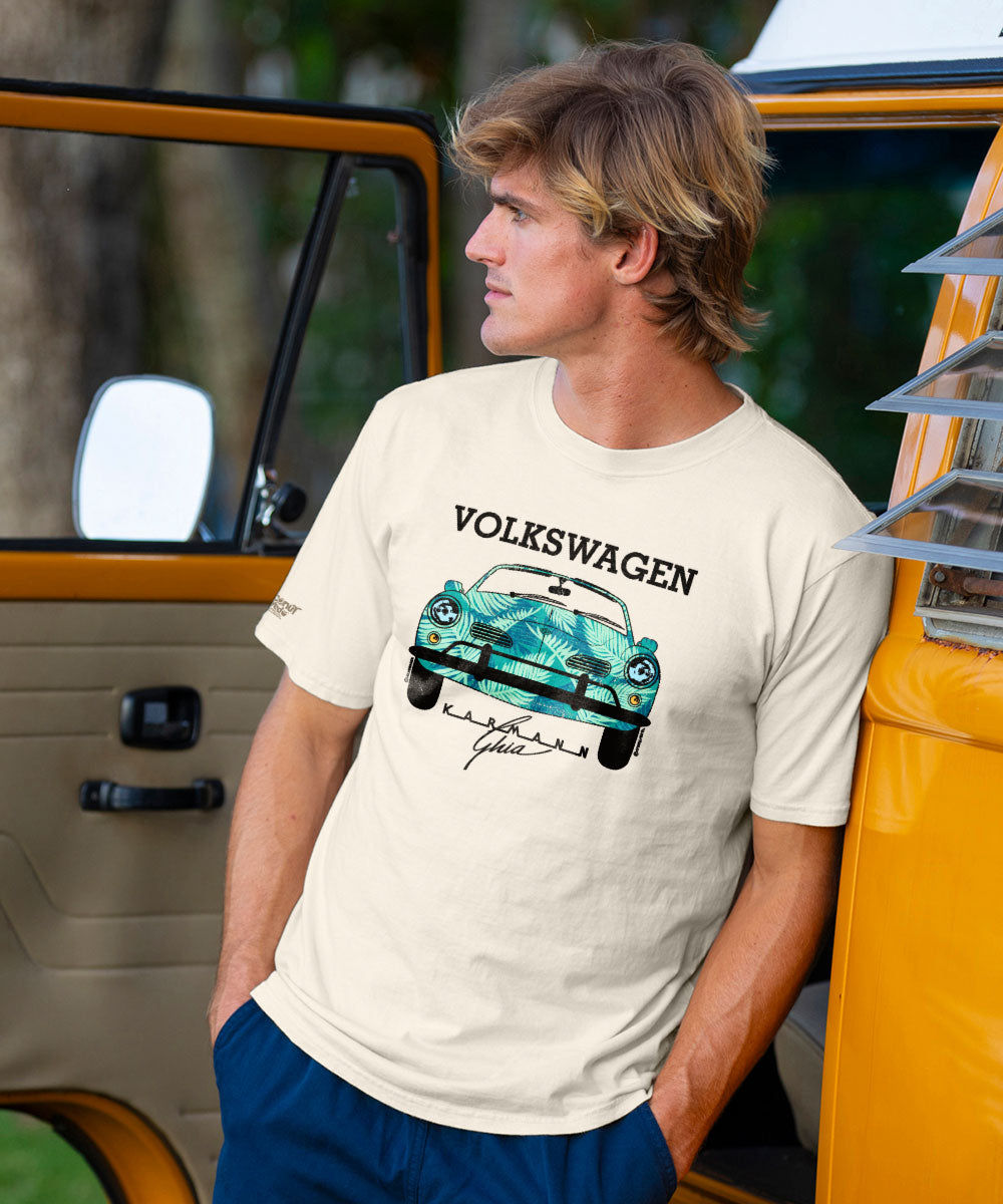 A person wearing a beige short sleeve crewneck t-shirt with a graphic of a Volkswagen Karmann Ghia car in a palm design. View 2