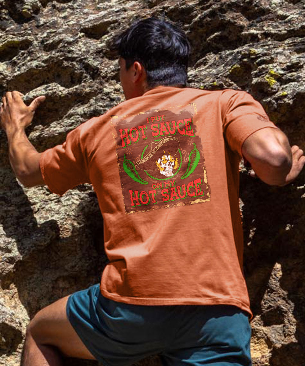 A person wearing a red short sleeve crewneck t-shirt with a hot sauce graphic on the back, climbing a rock wall. View 2
