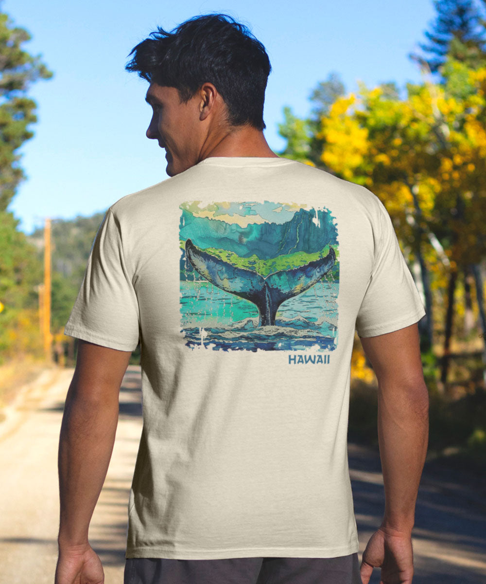 A person wearing a short sleeve crewneck t-shirt with a watercolor design of a whale tail, set against alorsevera background. View 2
