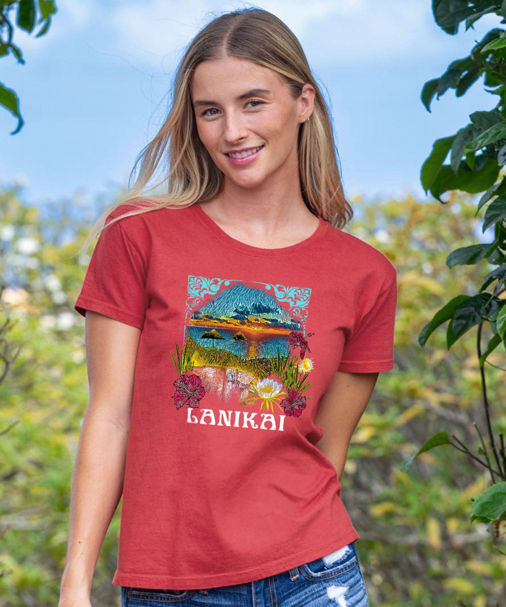 A woman wearing a red short sleeve crewneck t-shirt with a graphic of Lanikai and text, standing outdoors. View 2