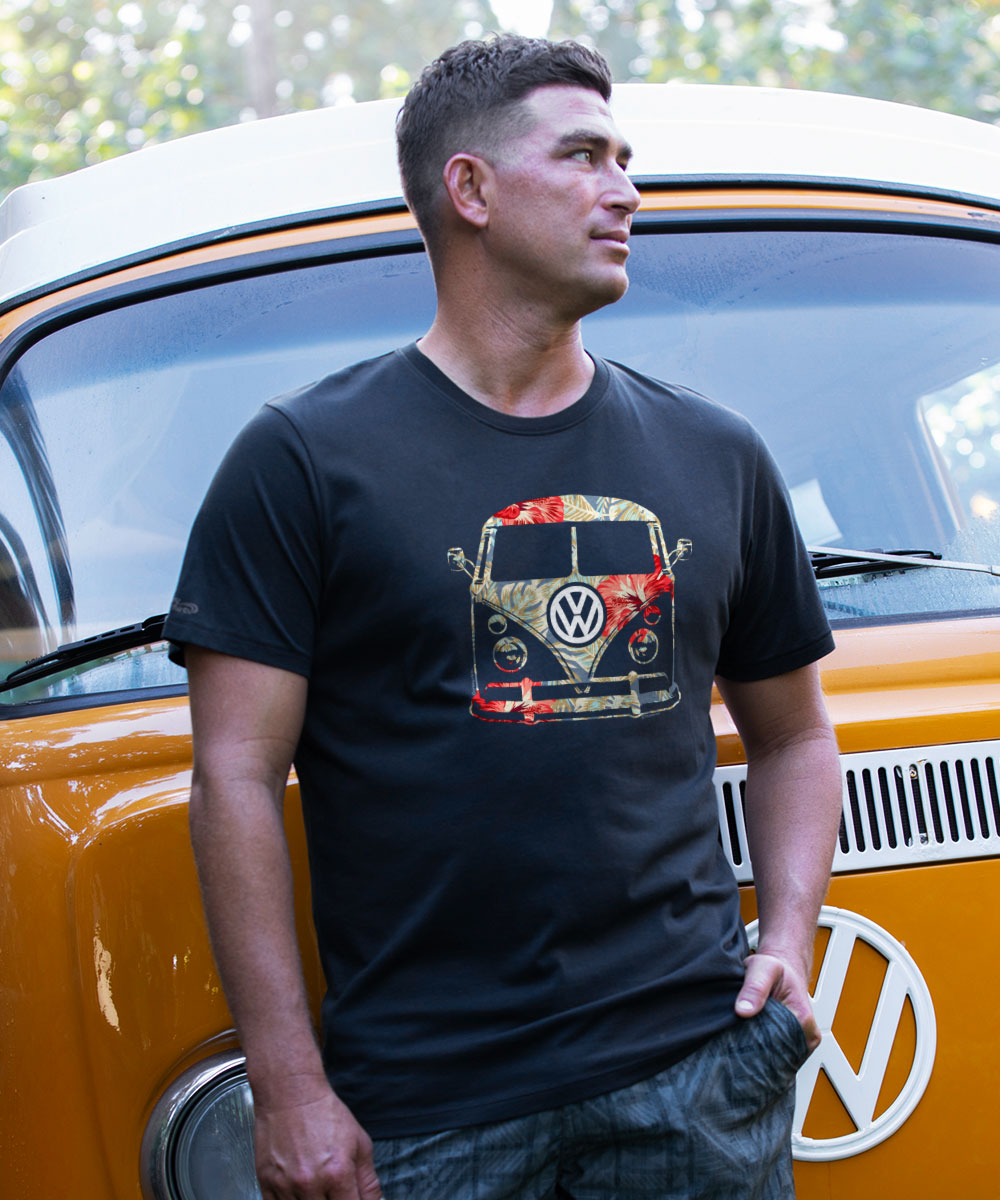 A man standing in front of a vintage yellow Volkswagen car, wearing a black short sleeve Pima cotton t-shirt with a graphic of a VW bus. View 2