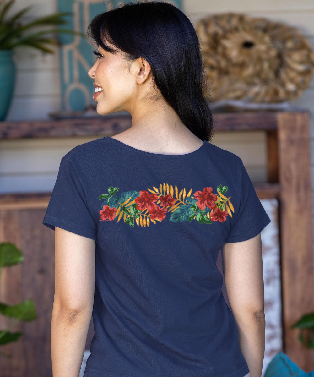 Woman wearing a navy blue t-shirt with floral design on the back, standing in a room with wooden furniture and plants. View 3