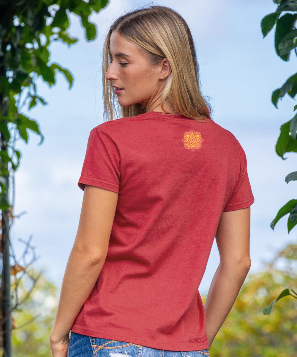 woman standing in a natural setting wearing a red t-shirt with a floral pattern on the back in blue jeans. View 3