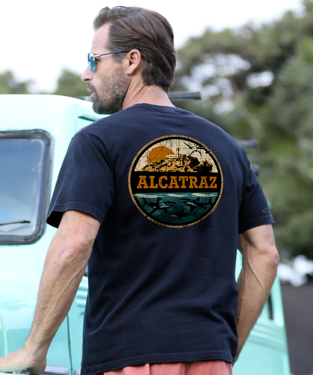 Man wearing a black t-shirt with 'Alcatraz' design, standing outdoors. View 2