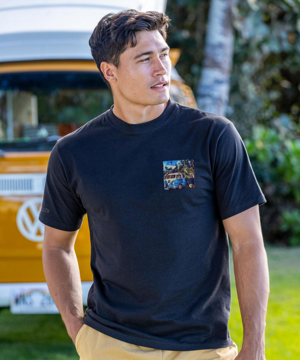 Man wearing a black t-shirt with a small graphic on a grassy area with a yellow vehicle in the background View 3