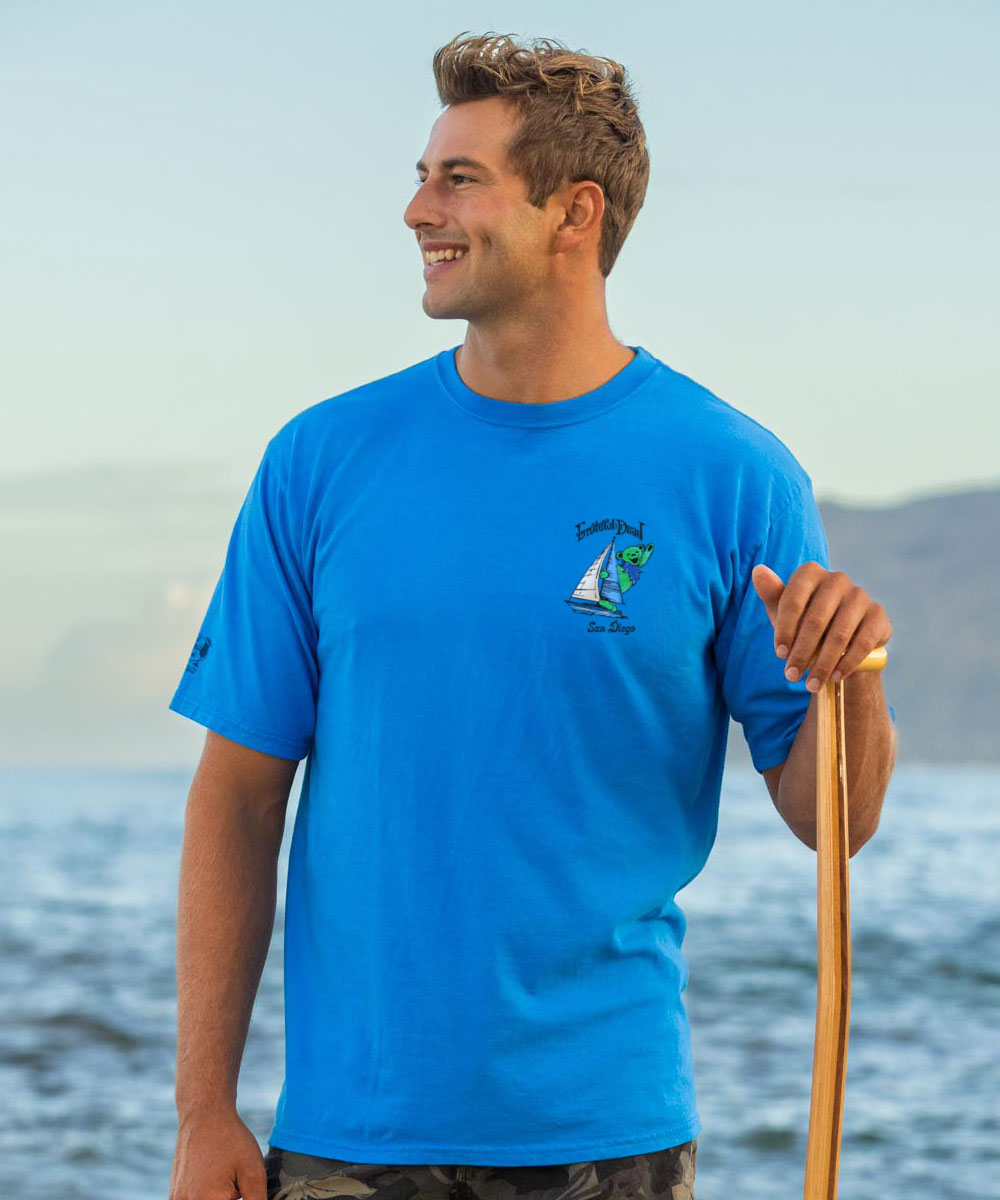 Man wearing a blue t-shirt with a sailboat design by a body of water View 3
