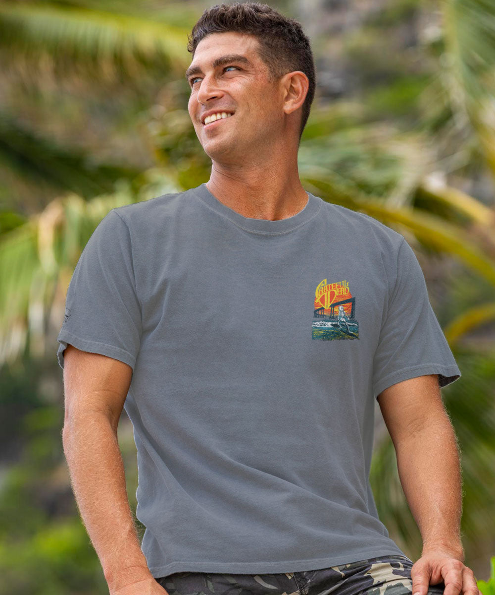 Man wearing a gray t-shirt with a pocket logo, standing outdoors with greenery in the background View 3