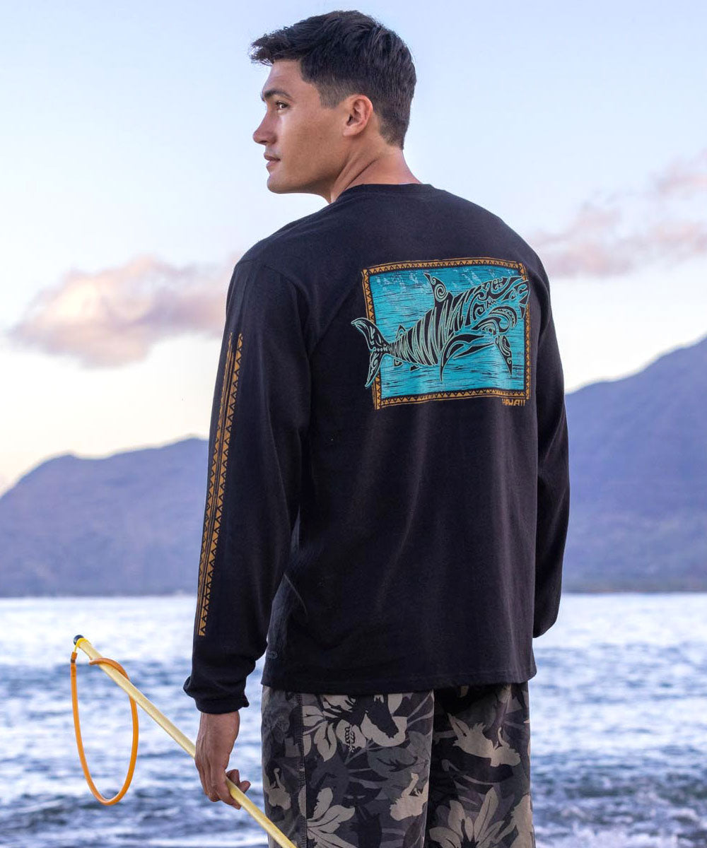 Man wearing a black long-sleeve shirt with a shark design by a body of water. View 2