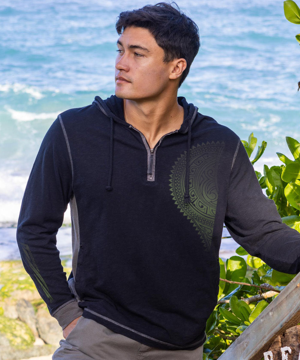 Man wearing a dark gray hoodie with a green tribal design by the ocean View 2