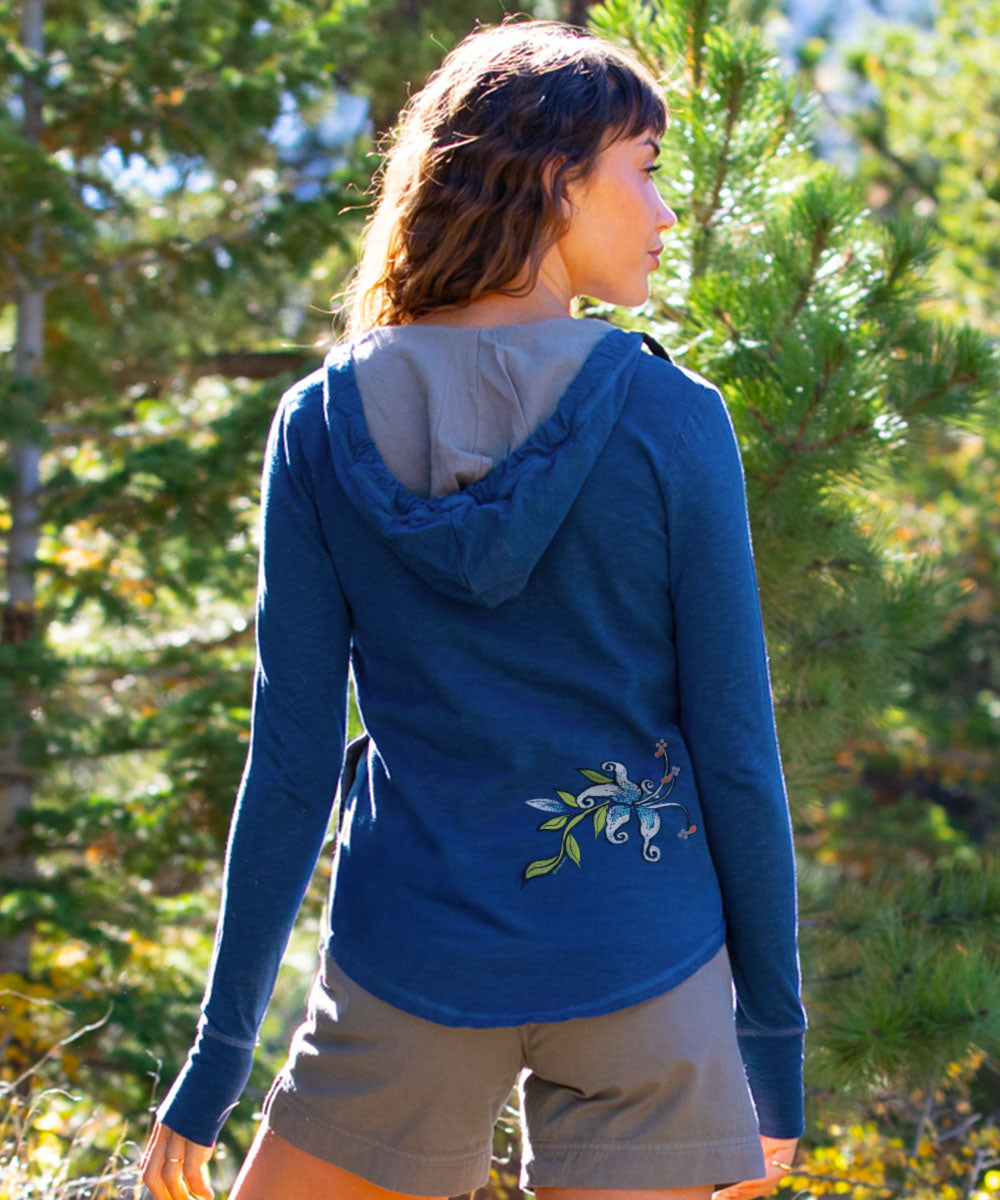 Woman wearing a blue hoodie with floral embroidery in a forest setting View 3
