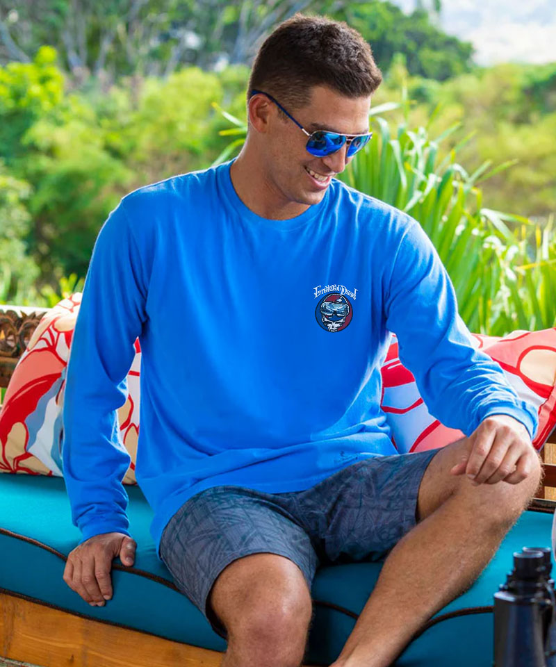 Man wearing a blue shirt with a logo, sitting outdoors with greenery in the background View 3