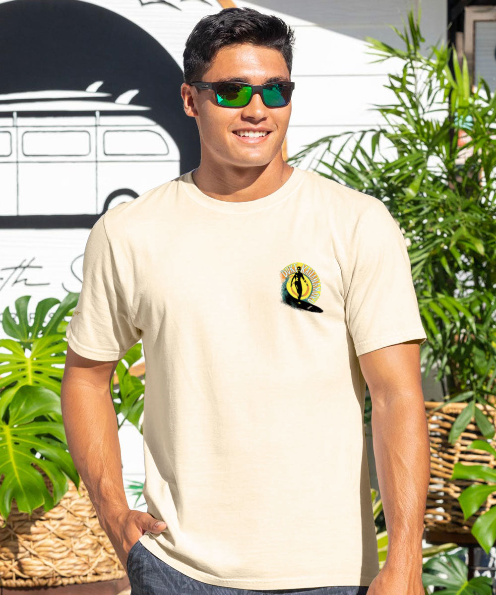 Man wearing a light beige t-shirt with a logo, standing outdoors. View 3