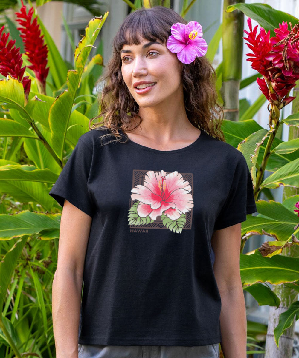 Woman wearing a black t-shirt with a pink flower design, standing in front of tropical plants. View 2
