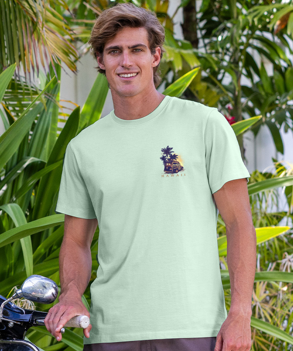 Man wearing a light green t-shirt with a logo, standing outdoors with greenery in the background View 3