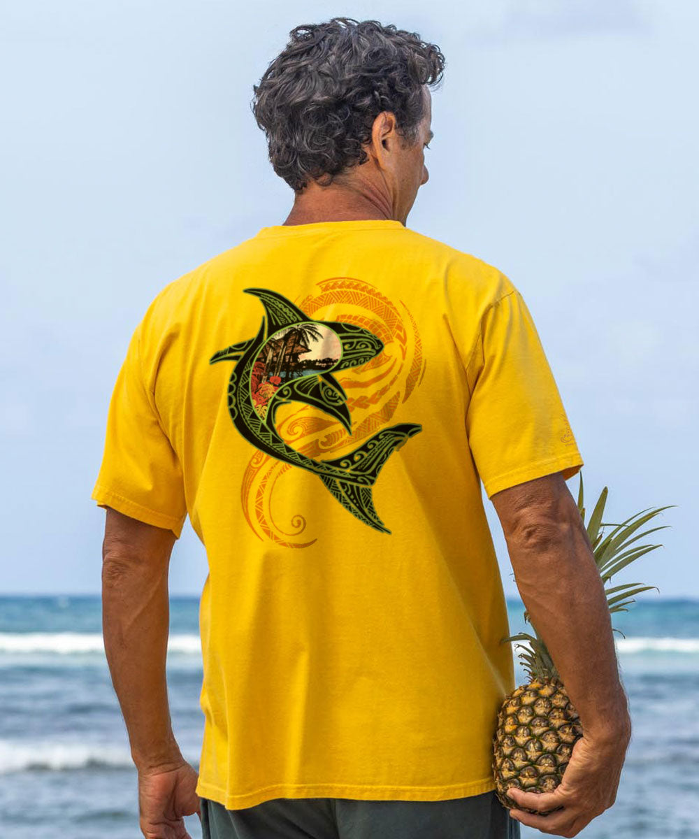 Man holding a pineapple, wearing a yellow t-shirt with a tribal shark design enjoying the beach View 2