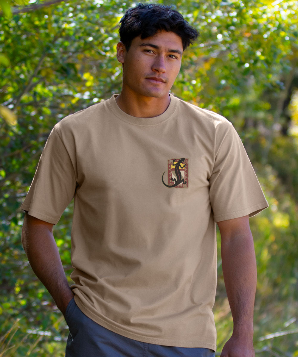 Man wearing a beige t-shirt with a logo in front of green foliage View 3