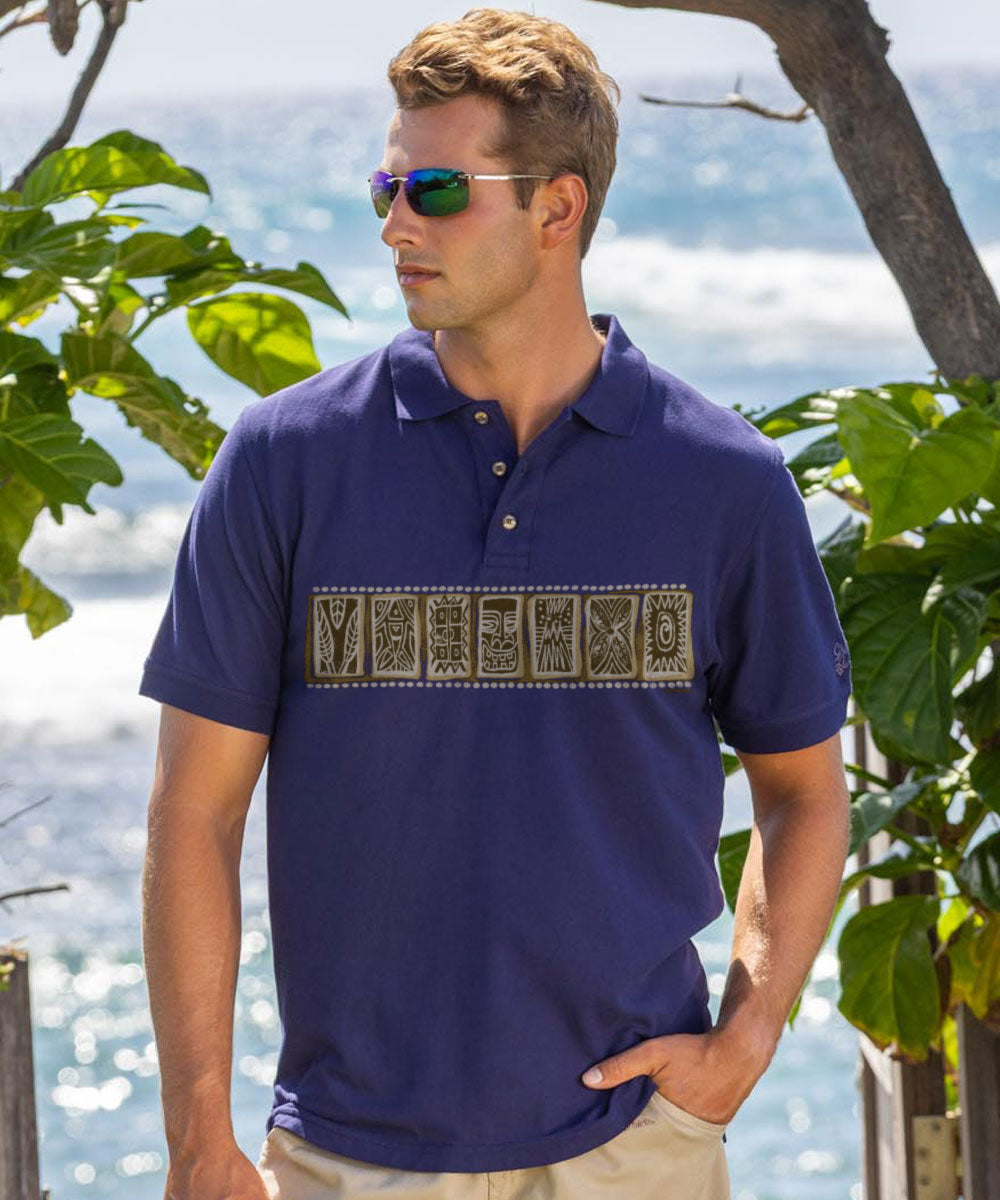 Man wearing a blue polo shirt with a graphic design, standing outdoors with greenery and water in the background. View 2