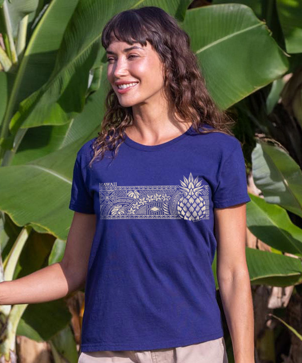 Woman wearing a blue t-shirt with a pineapple design in front of green foliage View 2