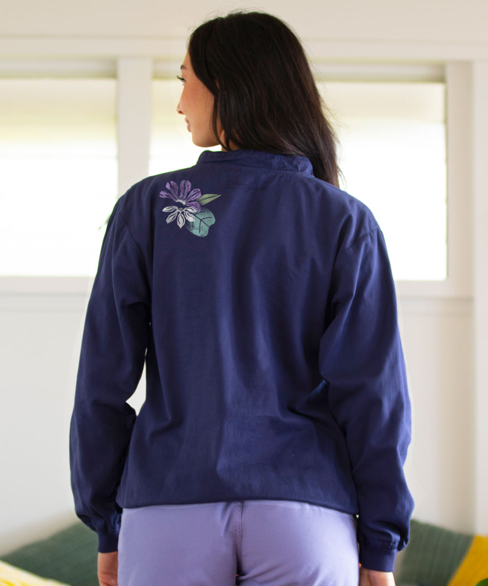 Person wearing a navy blue jacket with a floral design on the back, standing indoors. View 3