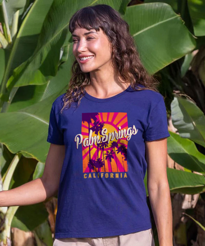 woman wearing a purple t-shirt with the text Palm spring california on it against a natural background. View 2