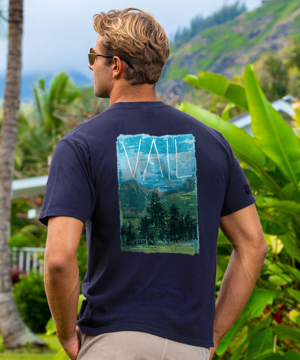 Man wearing a purple t-shirt with a scenic graphic on the back, standing outdoors with greenery around. View 2
