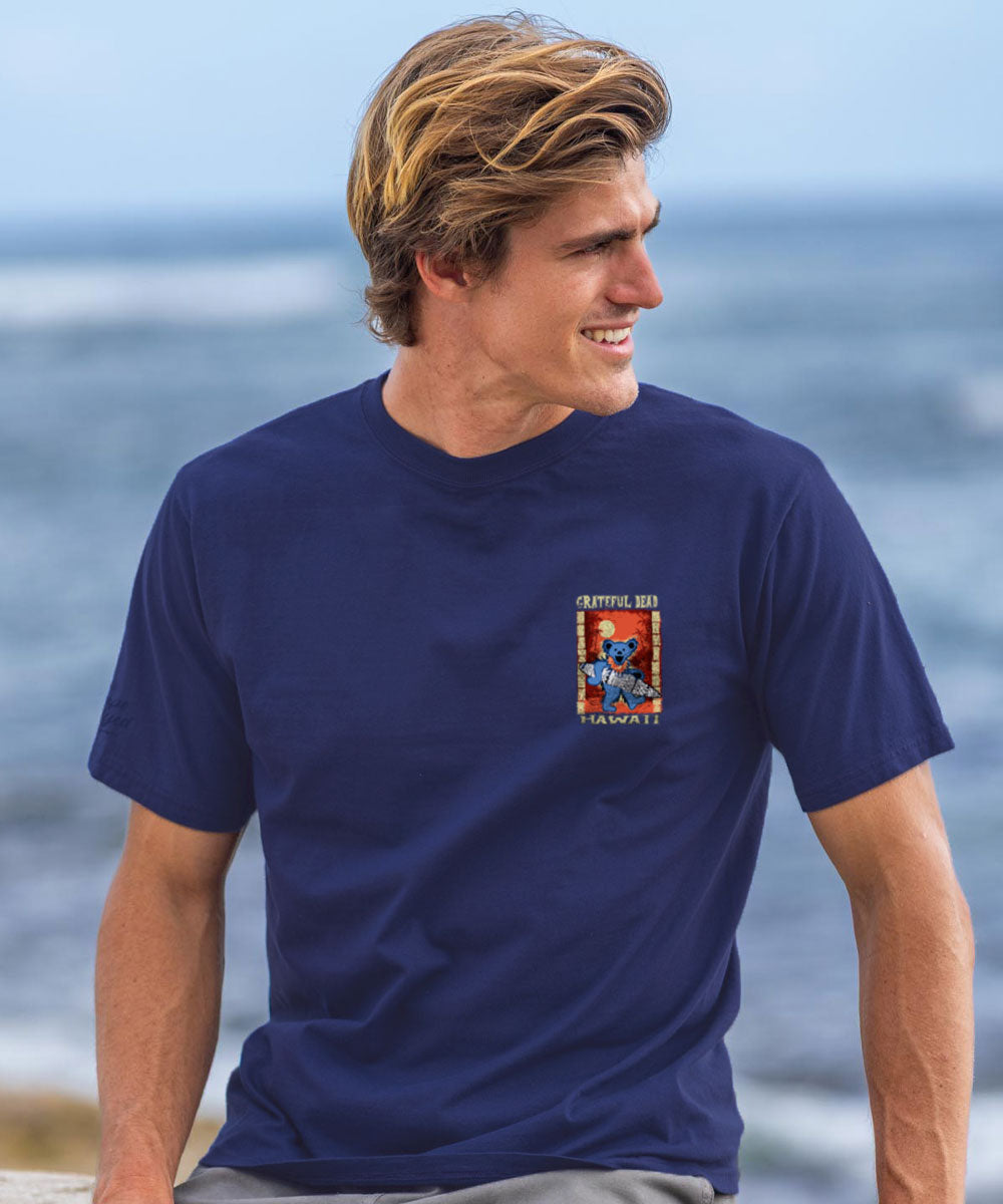 Man wearing a purple t-shirt with a pocket graphic design sitting by the ocean. View 3