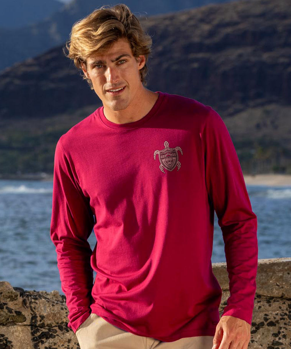 Man wearing a dark red long-sleeve shirt with a pocket logo, standing outdoors with mountains and water in the background. View 3