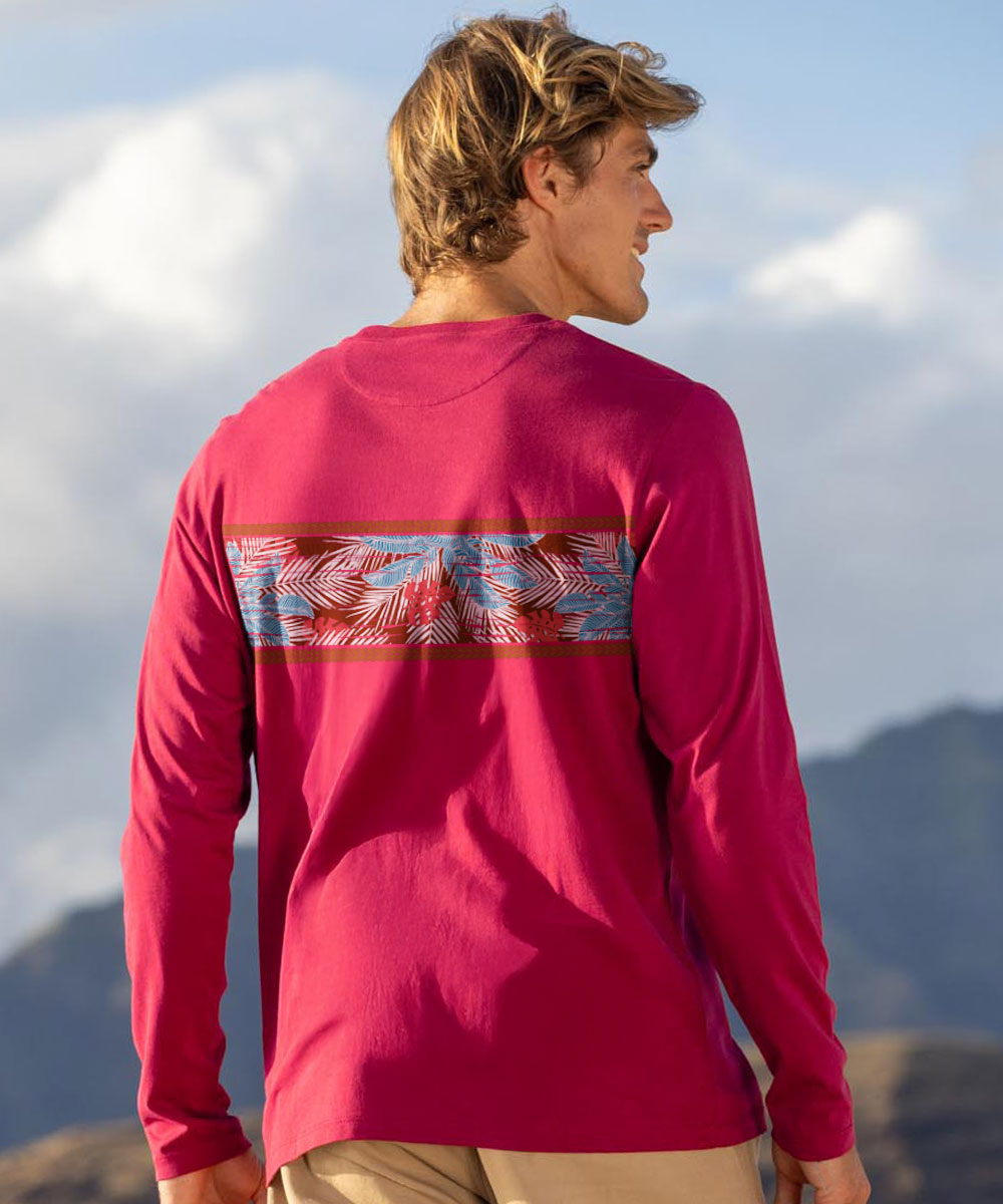 Man wearing a red long-sleeve shirt with a colorful design on the back, standing against a mountainous landscape. View 3