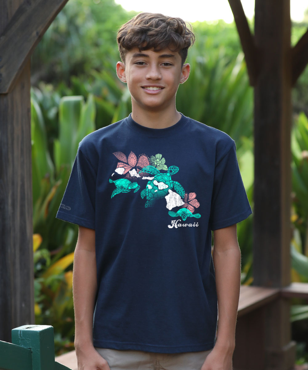 Young boy wearing a navy blue t-shirt with a colorful graphic design, standing outdoors with greenery in the background. View 2