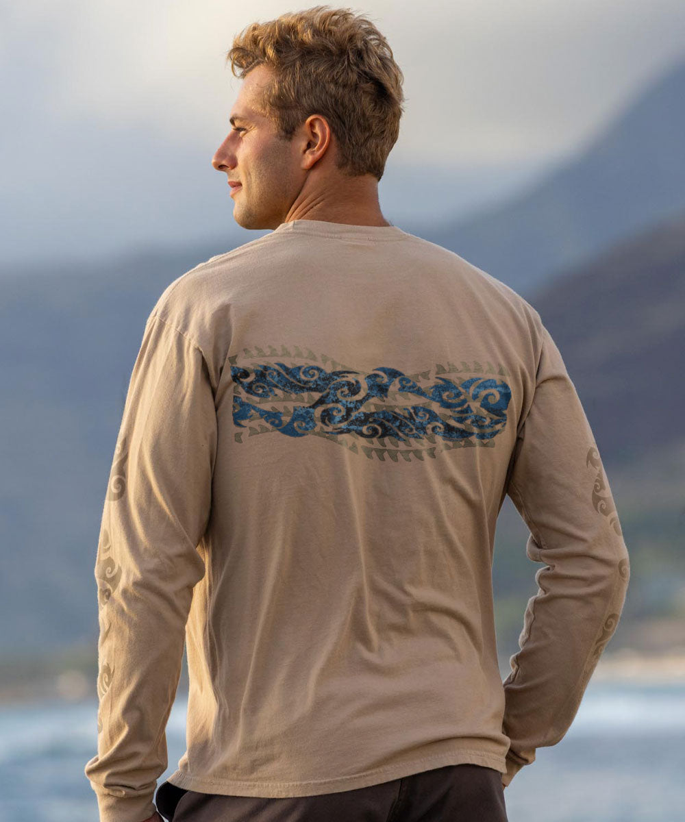 Man wearing a beige long-sleeve shirt with blue tribal graphic across the back, standing by a body of water with mountains in the background. View 3