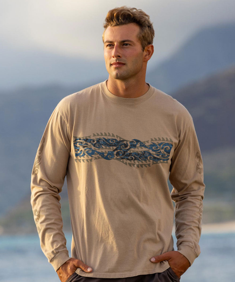 Man wearing a beige long-sleeve shirt with a blue pattern across the front, standing outdoors with mountains in the background. View 2