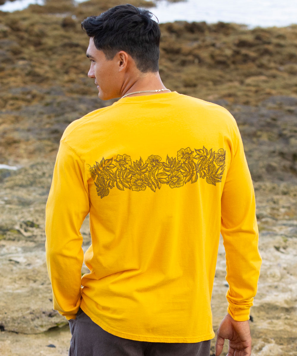 Person wearing a yellow long-sleeve shirt with a floral design on the back, standing on a rocky beach. View 3