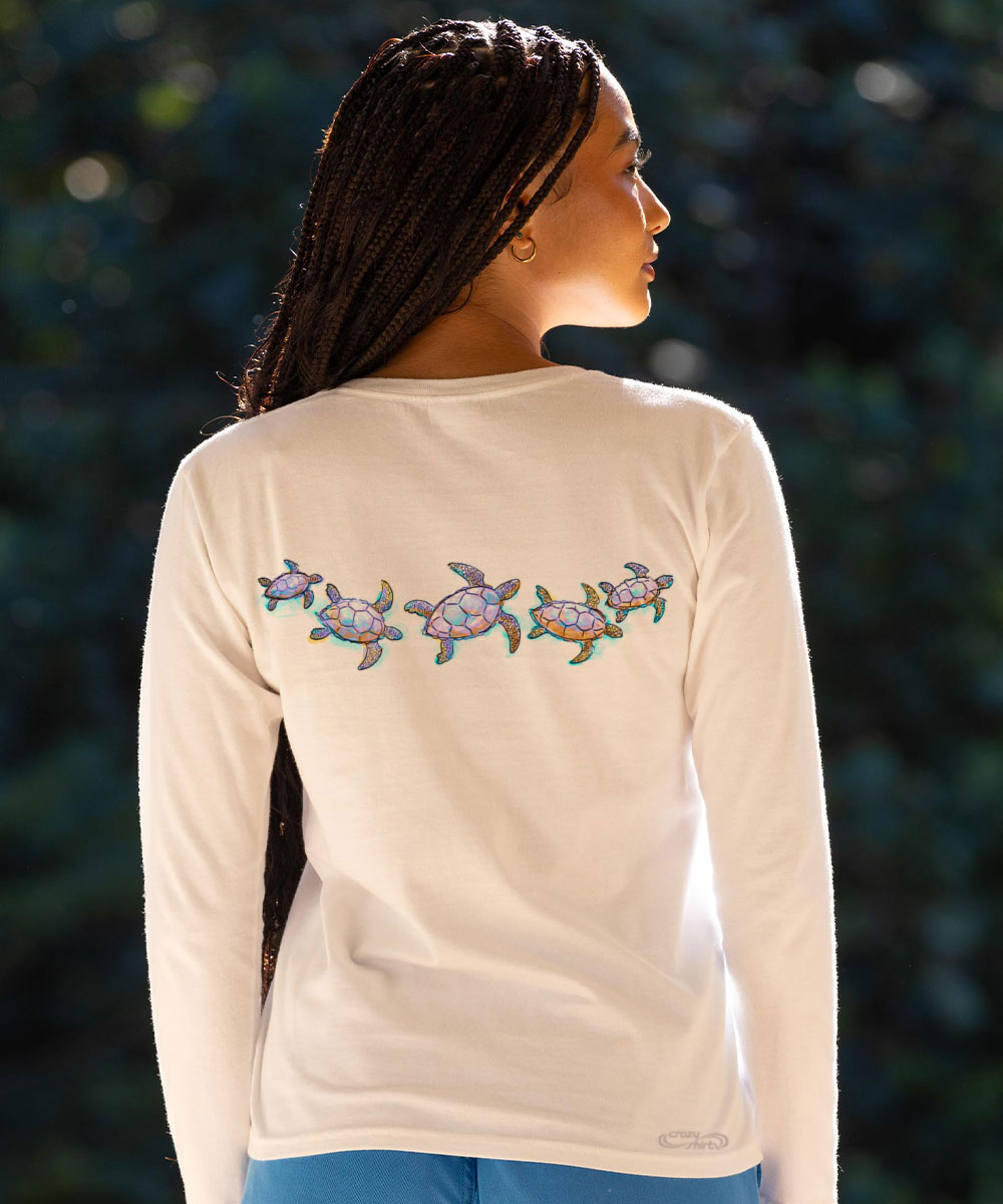 Woman wearing a cream long-sleeve shirt with turtle design on the back, standing against a blurred natural background. View 3