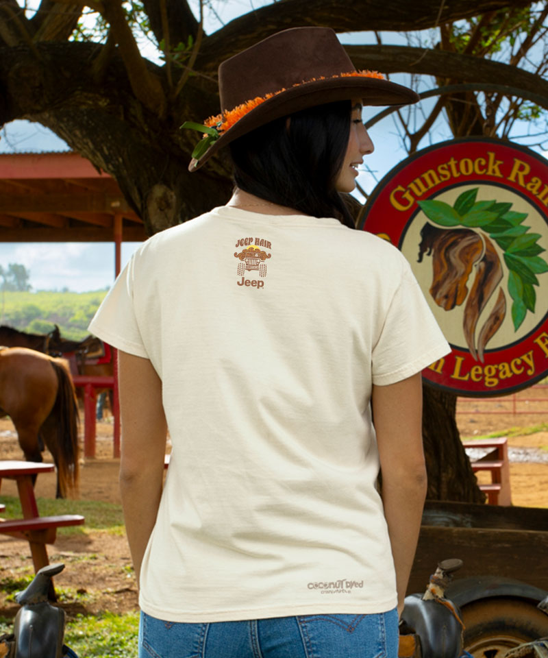 Person wearing a white t-shirt with branding in a rural setting with horses and a sign. View 3