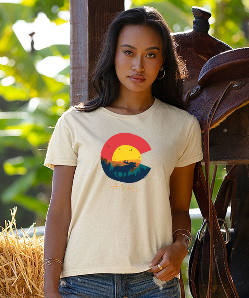 Woman wearing a t-shirt with a colorful logo in front of a horse and saddle. View 2