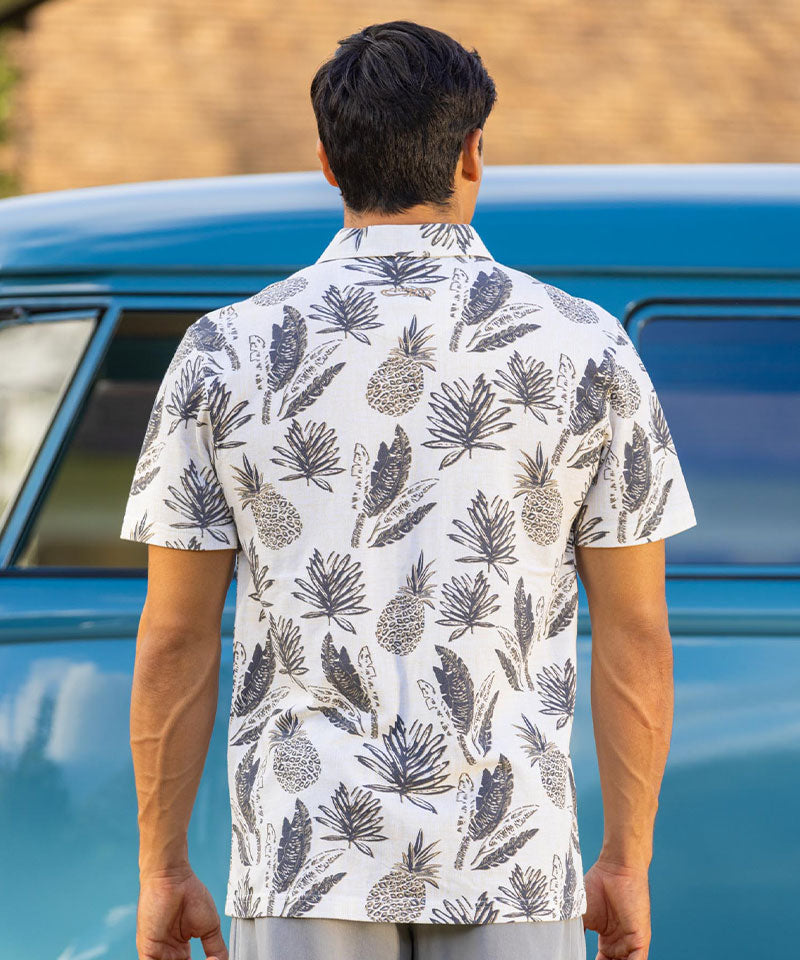 Man wearing a white patterned polo shirt standing in front of a vintage blue car. View 3