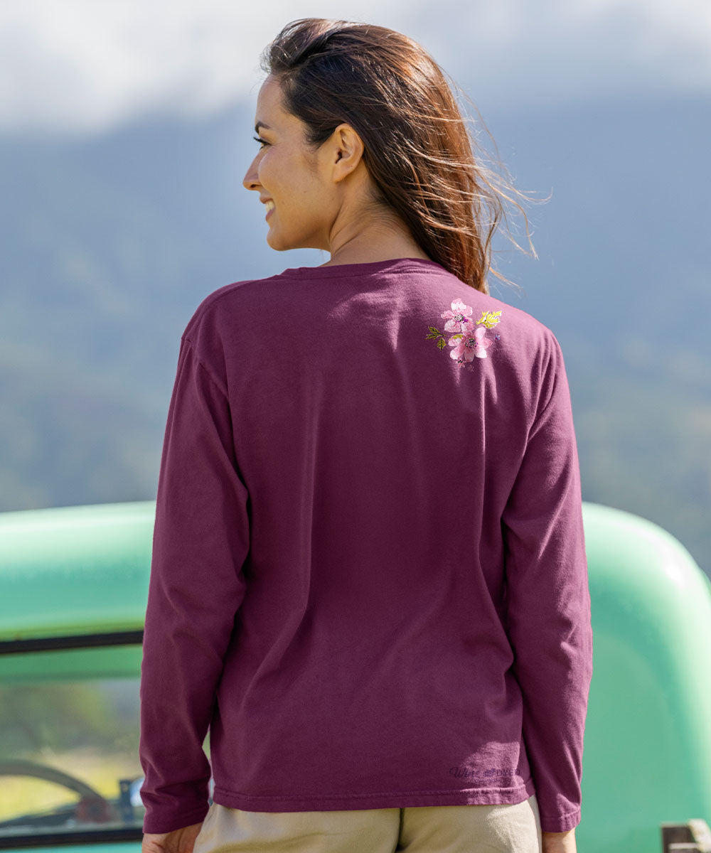 Woman wearing a purple long-sleeve shirt with a floral design on the back, standing outdoors with mountains in the background. View 3