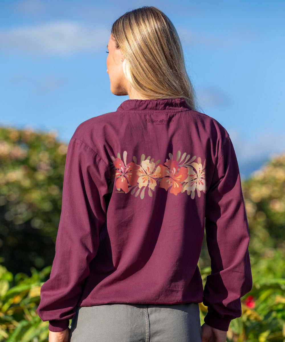 Person wearing a maroon jacket with floral designs on the back, standing outdoors with a blue sky and greenery in the background. View 3