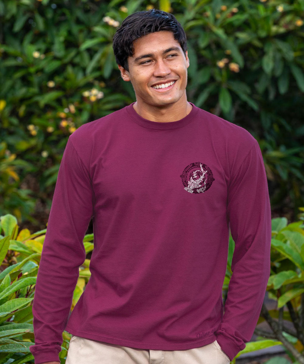 Man wearing a maroon long-sleeve shirt with a shark graphic pocket design, standing in front of green foliage. View 3
