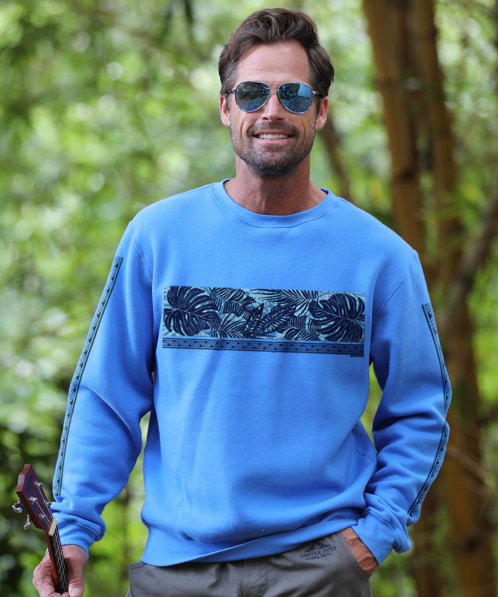 Man wearing a blue sweatshirt with a leaf pattern, holding a guitar, standing in a forest. View 2