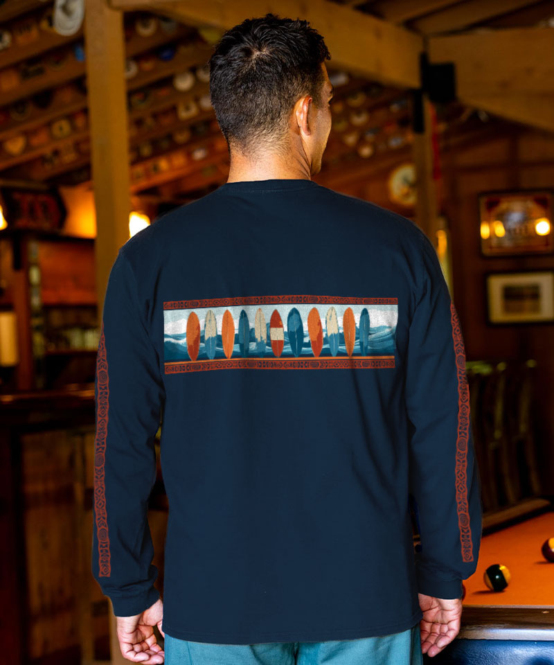 Man wearing a navy long-sleeve shirt with a colorful surfboard on the back, standing in a pool hall. View 3
