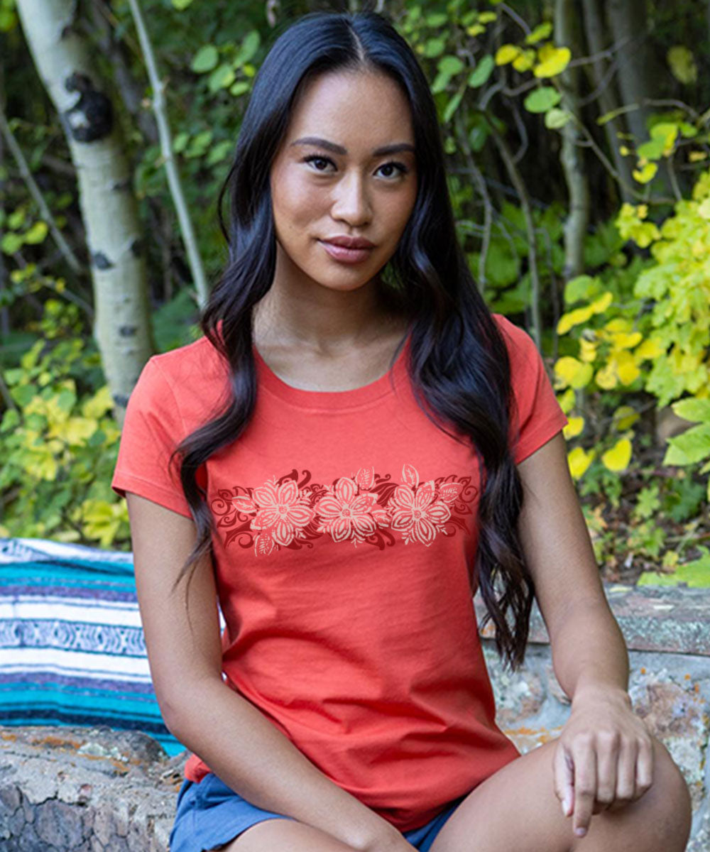 Woman wearing a red t-shirt with floral design sitting outdoors among greenery View 2