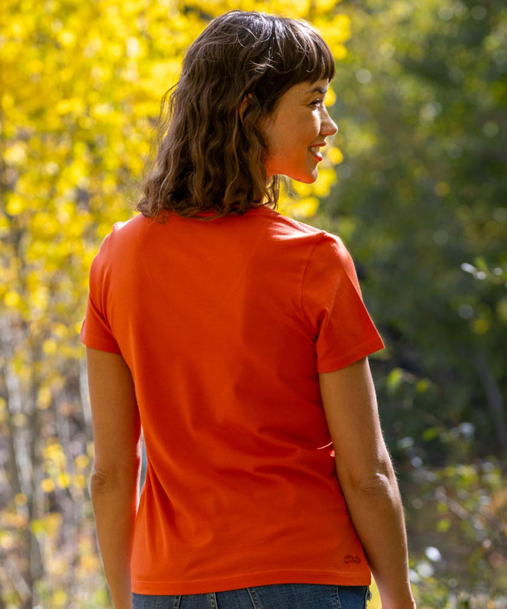 Woman wearing an orange t-shirt standing in a forest with autumn foliage. View 3