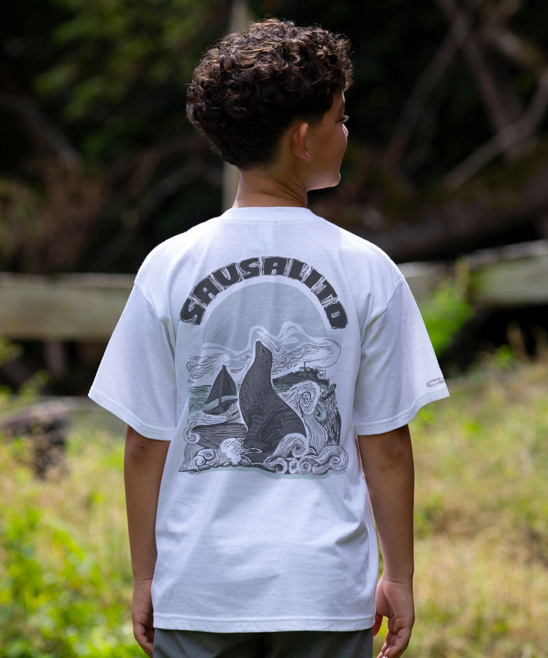 Person wearing a white t-shirt with a graphic design and text outdoors View 2