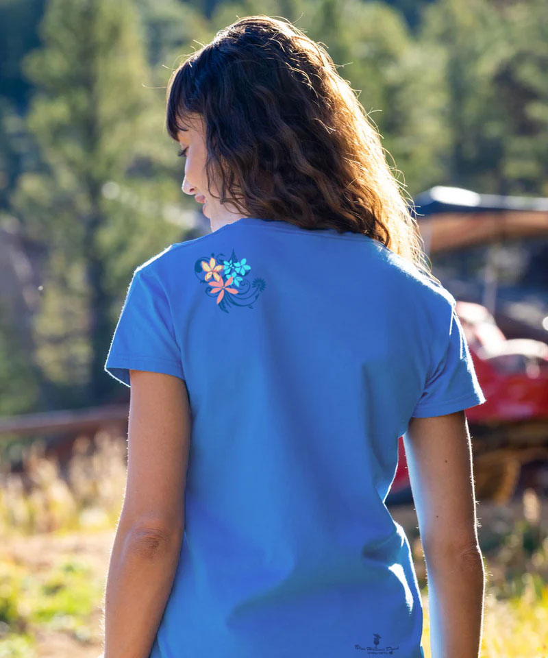 Person wearing a blue t-shirt with a floral design on the back, standing outdoors. View 3