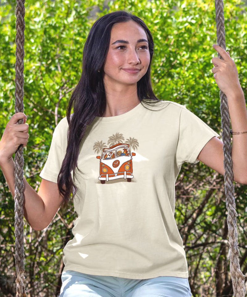 Woman wearing a white t-shirt with a graphic design of a van and palm trees, sitting on a swing with greenery in the background. View 3