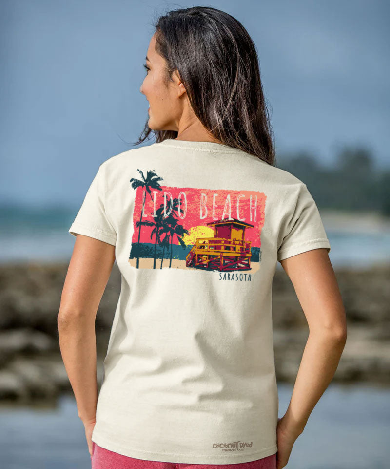 Woman wearing a t-shirt with a beach graphic on the back, standing by a body of water. View 2