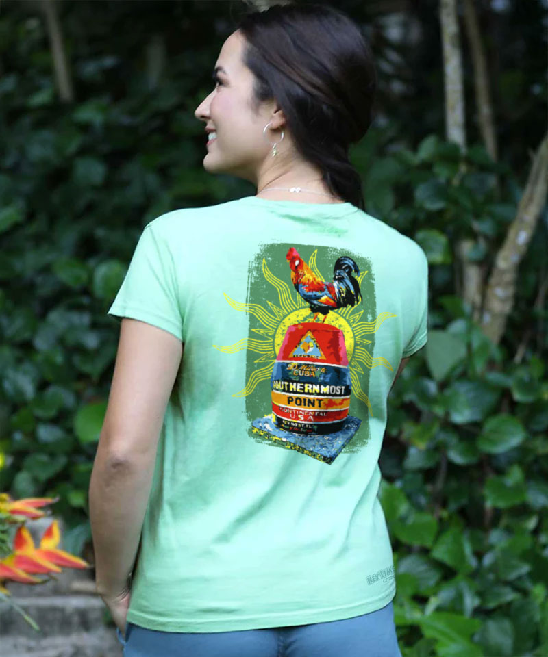 Person wearing a light green t-shirt with a colorful graphic on the back, standing in a natural setting. View 3