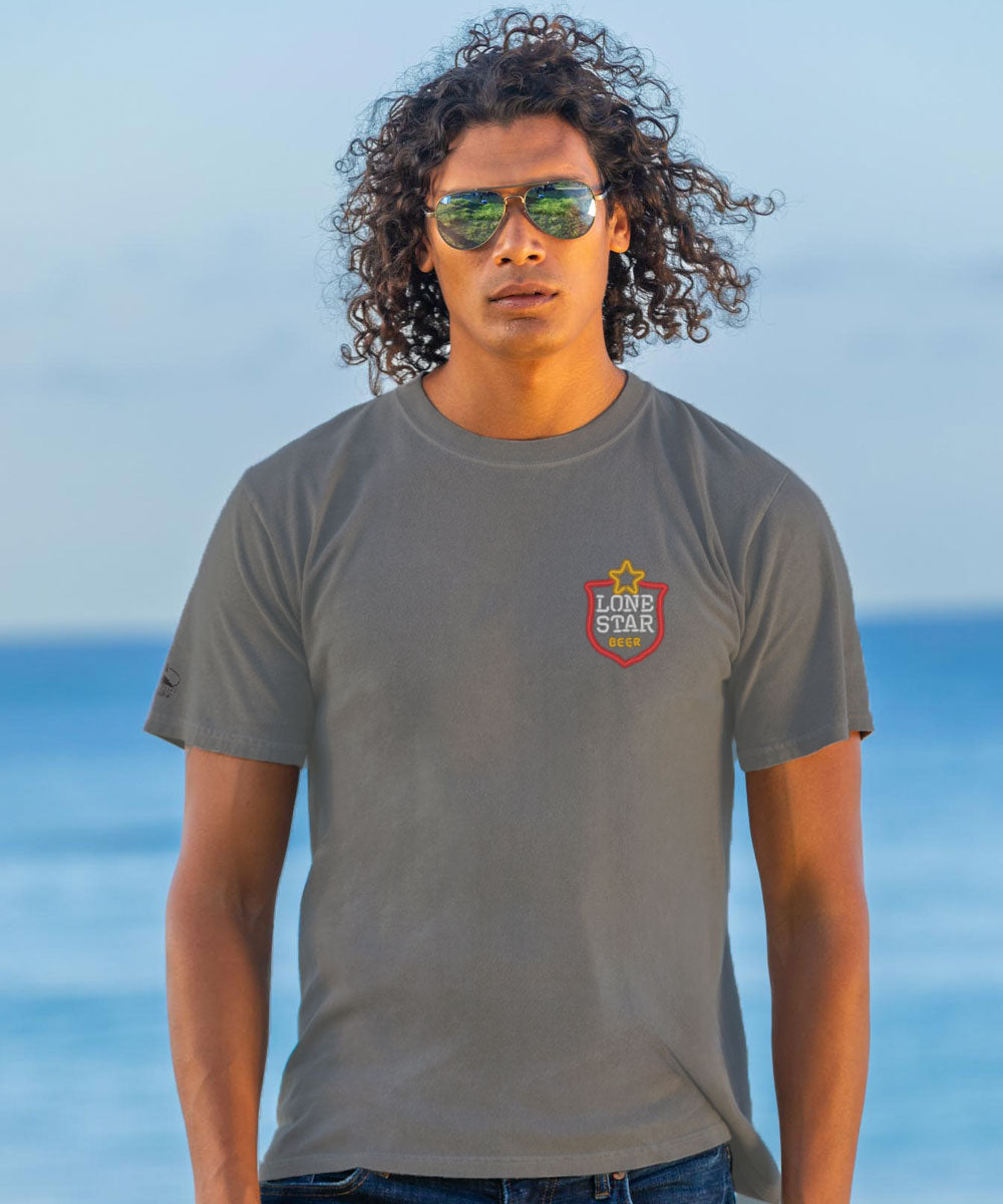 Man wearing a gray t-shirt with a logo on the chest, standing against a blue sky. View 3