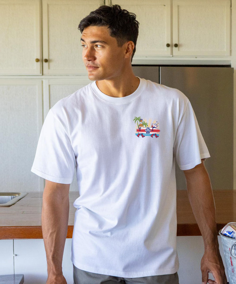 Man wearing a white t-shirt with a small colorful graphic logo in a kitchen View 3